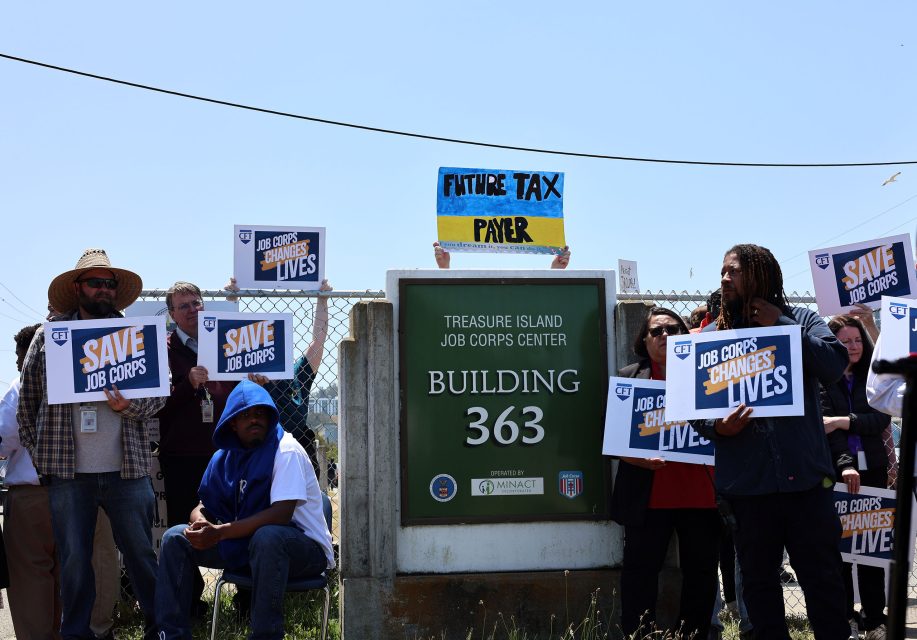 A group of people hold signs reading "SAVE JOB CORPS" and "JOB CORPS CHANGES LIVES" outside the Treasure Island Job Corps Center, Building 363.