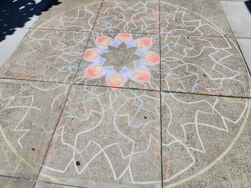Chalk mandala with geometric patterns and colorful shapes drawn on a concrete sidewalk.