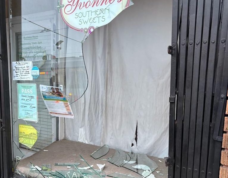 A shattered storefront window with broken glass on the ground. The sign reads "Yvonne's Southern Sweets." The interior is blocked by a white sheet.