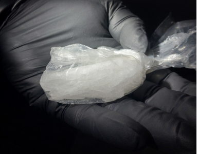 A gloved hand holds a clear plastic bag containing a white, crystalline substance.