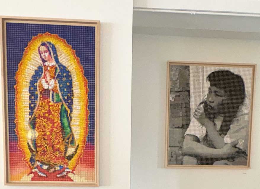 Two framed artworks hang on a white wall: one depicts Our Lady of Guadalupe in vibrant colors, the other shows a grayscale portrait of a person resting their chin on their hand.