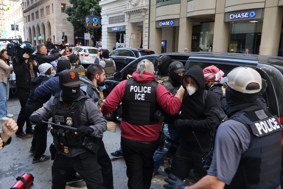 Police officers in tactical gear with "POLICE ICE" vests detain several individuals during a street confrontation near a Chase bank branch.