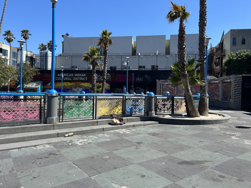 A paved plaza with palm trees, colorful railings, and a building labeled "American Indian Cultural District" under a clear blue sky.