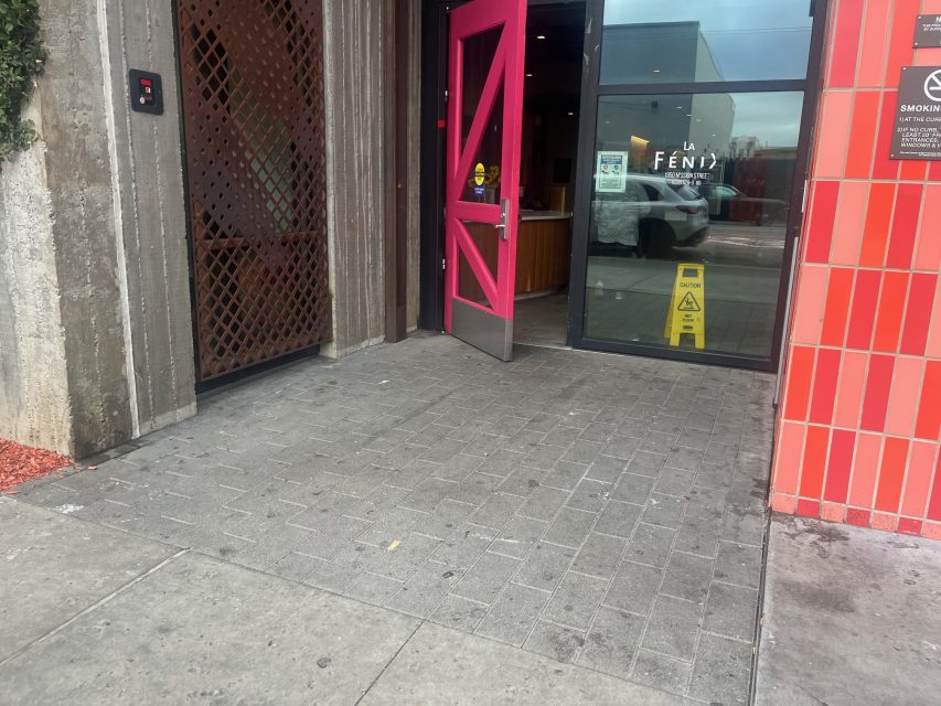 An open pink door leads into Yvonne's building, with a caution wet floor sign inside near the entrance. "La Fenty" is visible on the glass in the background.