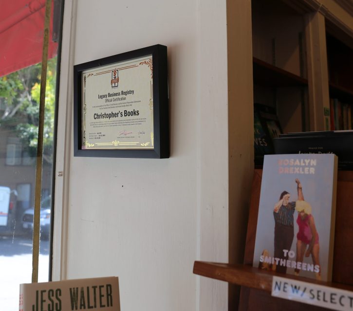 A framed certificate for Christopher's Books hangs on a wall near a window; a bookshelf with various books and a mail truck outside are visible.