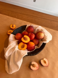 A black bowl lined with a white cloth holds several whole nectarines, with halved nectarines placed on the brown tabletop nearby.