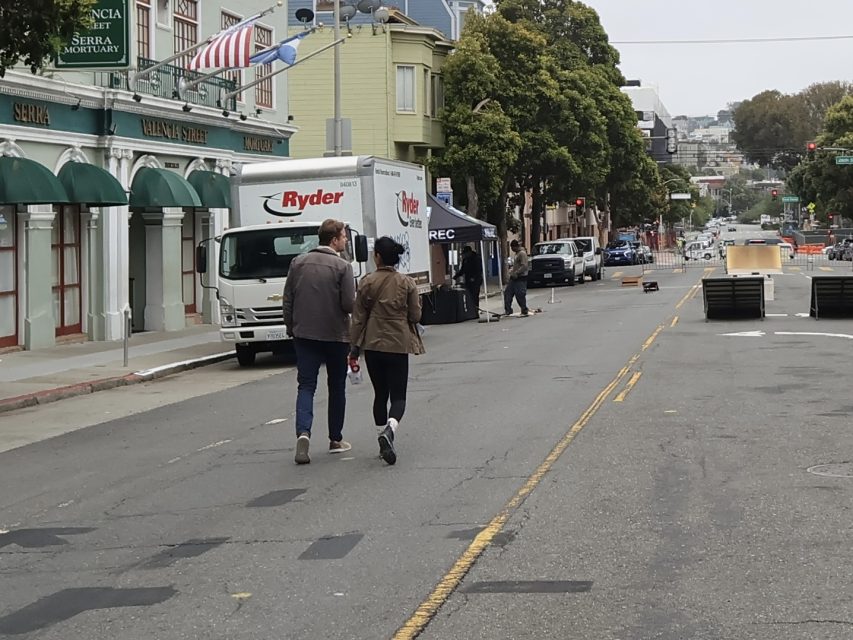 Two people walk down a city street closed to traffic, passing by a Ryder truck and tents set up along the sidewalk.