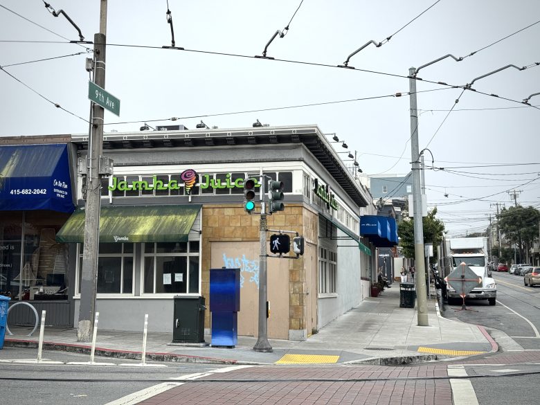 Street corner with a Jamba Juice store, traffic lights, crosswalk, and overhead power lines. A street sign reads "9th Ave" and there are cars parked along the curb.