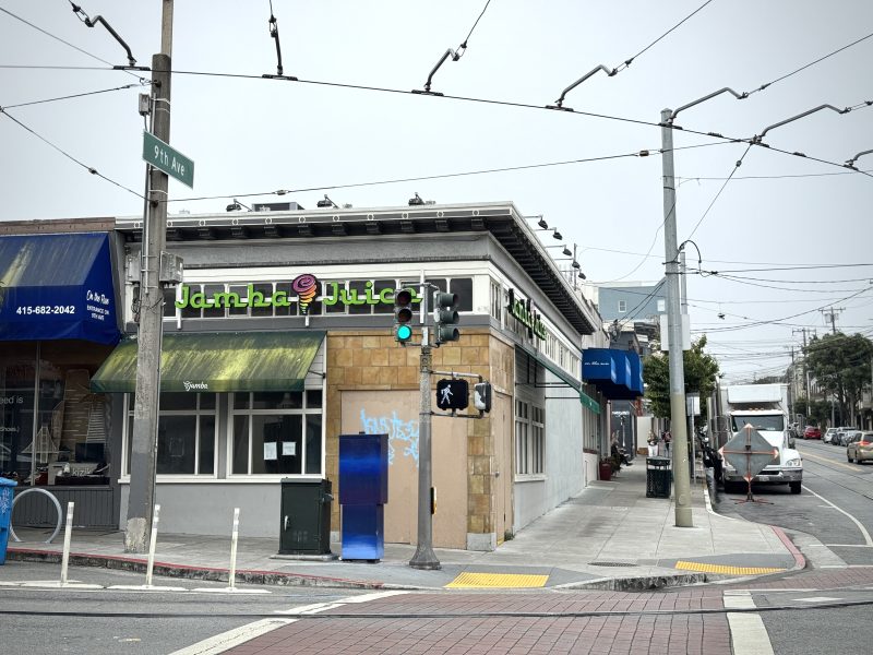 Street corner with a Jamba Juice store, traffic lights, crosswalk, and overhead power lines. A street sign reads "9th Ave" and there are cars parked along the curb.