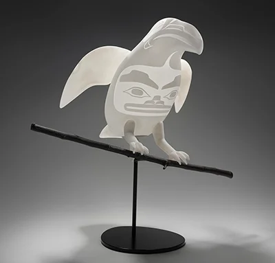 Translucent bird sculpture with stylized Indigenous artwork on its body, perched on a horizontal rod and mounted on a round black base.