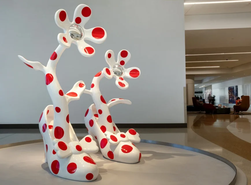 Large white high-heeled shoe sculptures with red polka dots and flower-like extensions are displayed in a modern lobby area.
