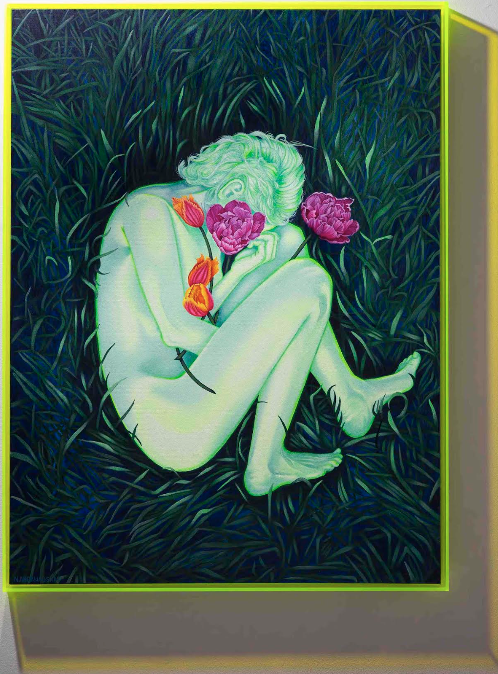 A pale, nude figure lies curled on green grass with vibrant flowers blooming from their head and body, depicted in a neon-framed painting.