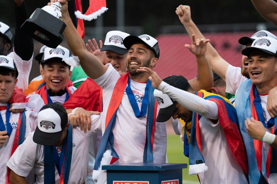 A soccer team wearing white shirts and caps celebrates on the field, with one player holding a trophy aloft and others cheering around him—capturing the spirit of El Farolito's triumph.