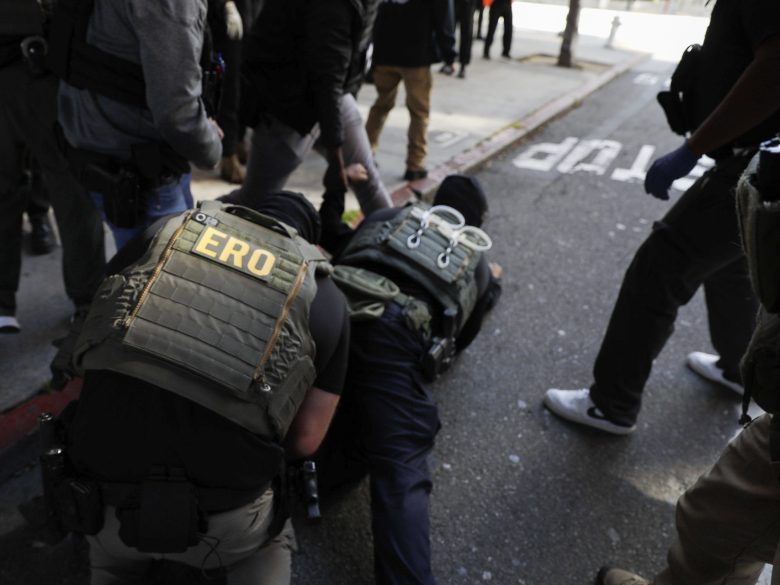 Law enforcement officers detain a person on the ground during an operation on a city street.