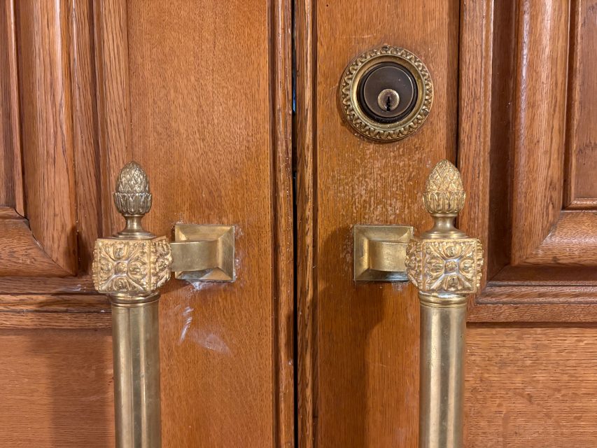 Close-up of double wooden doors with ornate brass handles and a round deadbolt lock above the handles.
