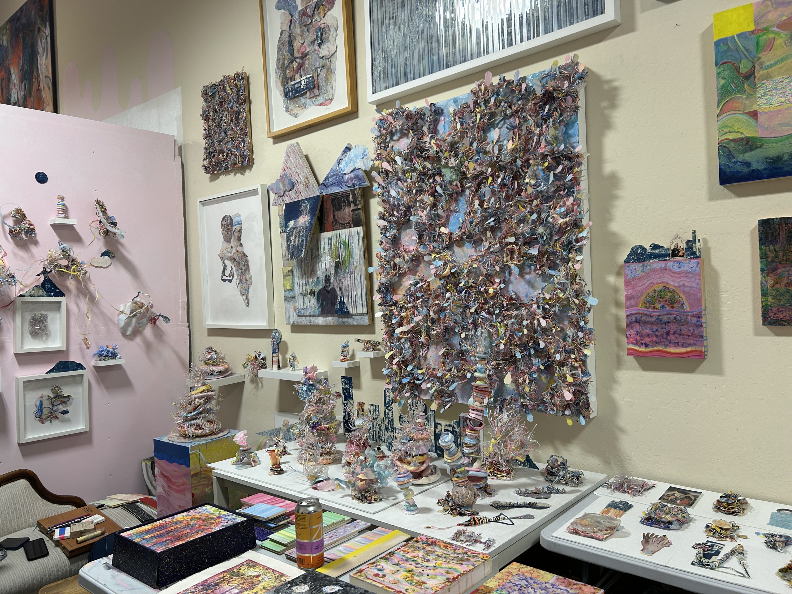 Art studio with walls and tables filled with colorful mixed-media sculptures, textured wall art, framed paintings, and art supplies—perfect for exploring during an inspiring local art walk.