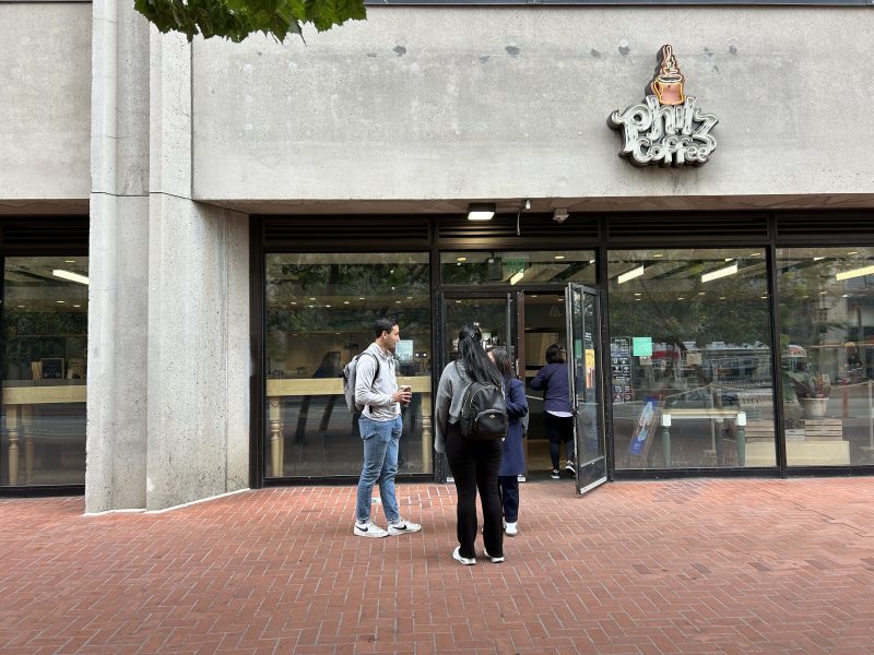 Three people stand outside Phin Coffee, a café with glass doors and windows, while another person enters the shop.