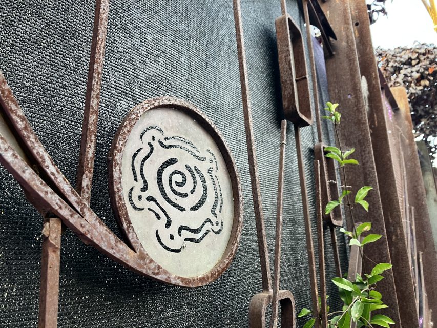 Close-up of a rusty metal gate featuring a circular decorative pattern, with green plant leaves growing nearby.