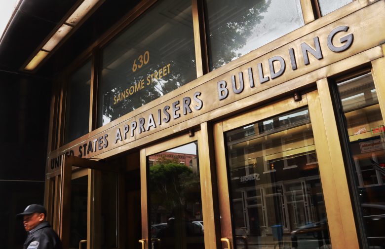 The entrance of the United States Appraisers Building at 630 Sansome Street, with a security guard walking by.
