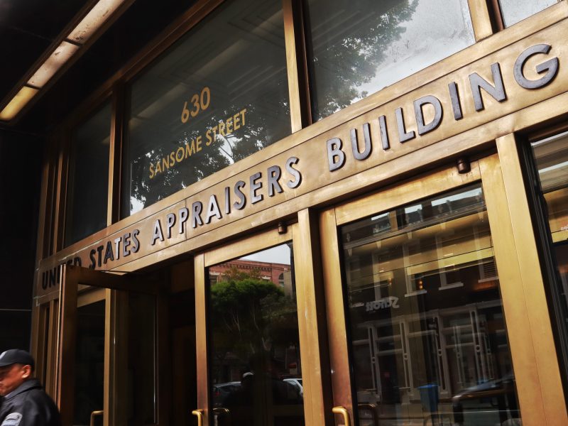 The entrance of the United States Appraisers Building at 630 Sansome Street, with a security guard walking by.