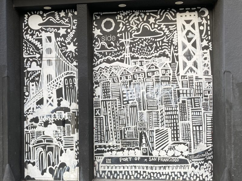 Black and white mural depicting San Francisco landmarks, including bridges and city buildings, with abstract patterns and text on a building wall.