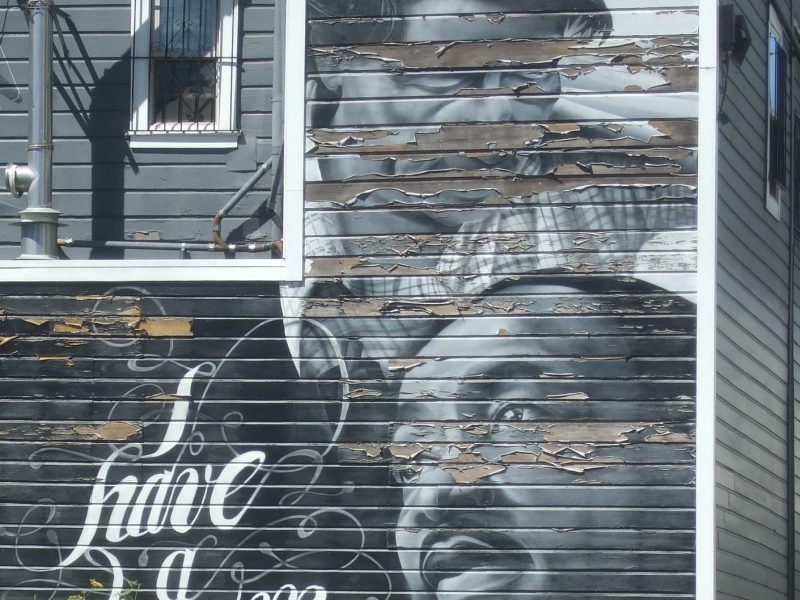 Black and white mural on a wooden building featuring Martin Luther King Jr., a child, and the words "I have a dream;" some paint is peeling.