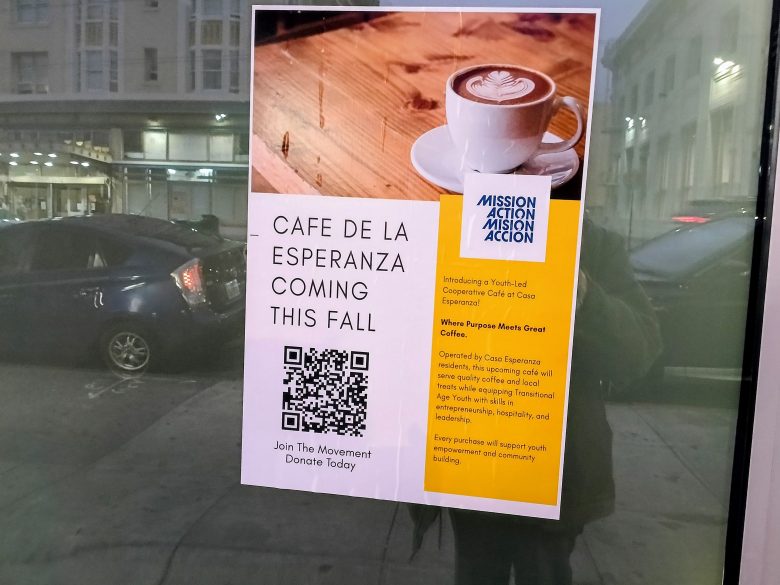 A flyer on a window announces the upcoming Cafe de la Esperanza, with a coffee cup image, QR code, and details about the cafe’s mission and fall opening.