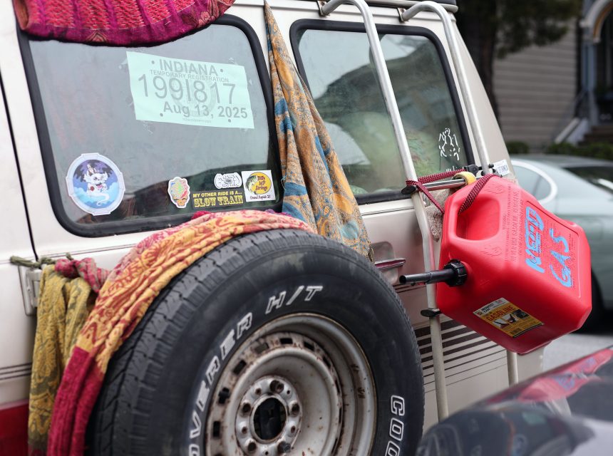 Rear view of a vehicle with an Indiana temporary license plate, a spare tire, blankets, various stickers, and a red gas can mounted on the back.