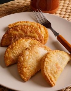Four fried empanadas arranged on a white plate with a fork placed to the side, on a woven placemat background.
