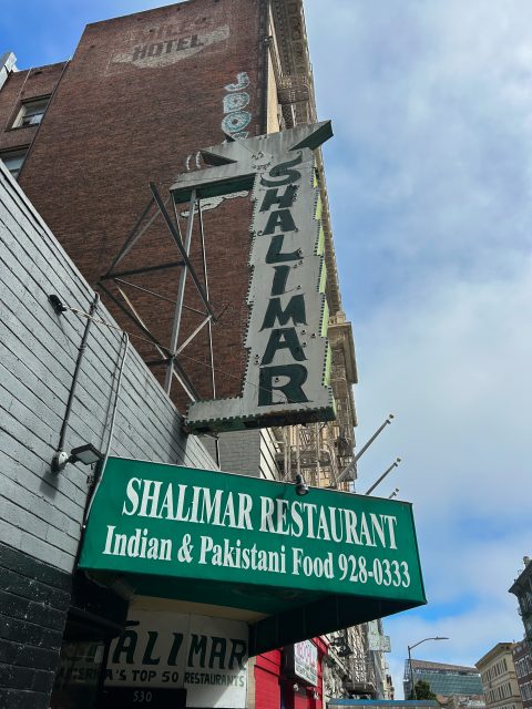 A green sign reads "Shalimar Restaurant, Indian & Pakistani Food, 928-0333" under an older vertical sign for "Shalimar" on a city street.