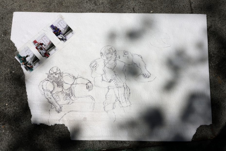 A rough pencil sketch of two American football players on a torn white sheet, with three photo references of players attached to the upper left corner.