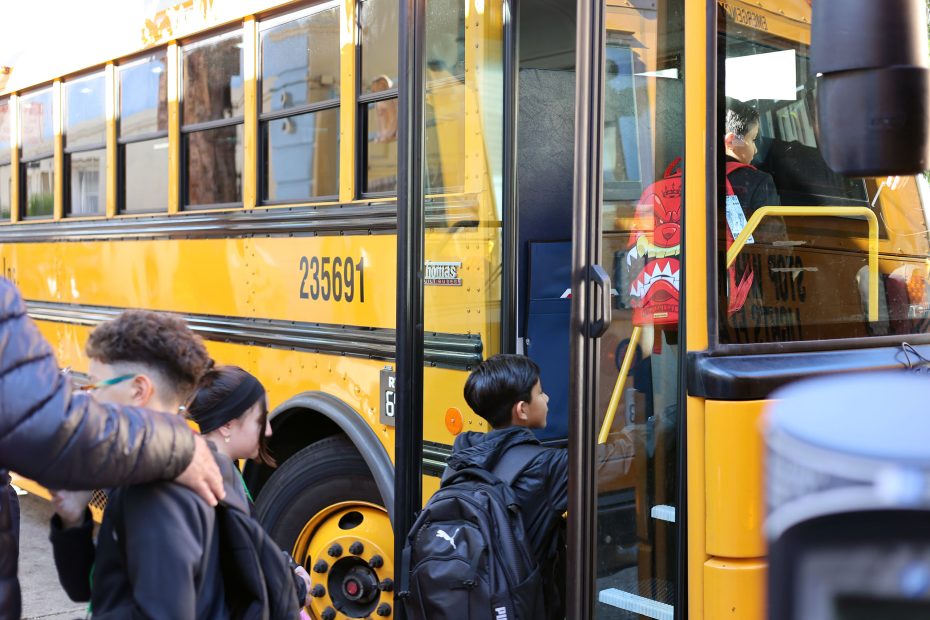 Children with backpacks board a yellow school bus numbered 235691, while an adult stands nearby.