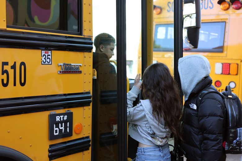 Two students wait to board a yellow school bus while another student steps inside through the open door.