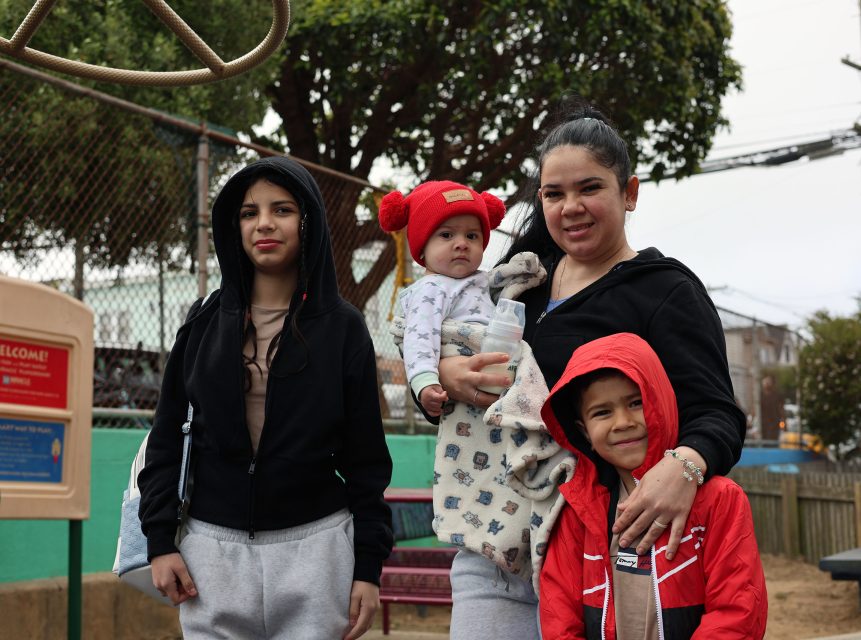 A woman and three children pose together at an outdoor playground on a cloudy day. The children are dressed in warm clothing.