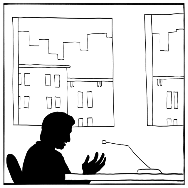 A person sits at a desk speaking into a microphone, silhouetted against large windows showing buildings outside.