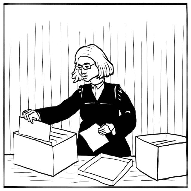 A person with glasses is standing at a table, sorting through files in a box with another open box nearby.