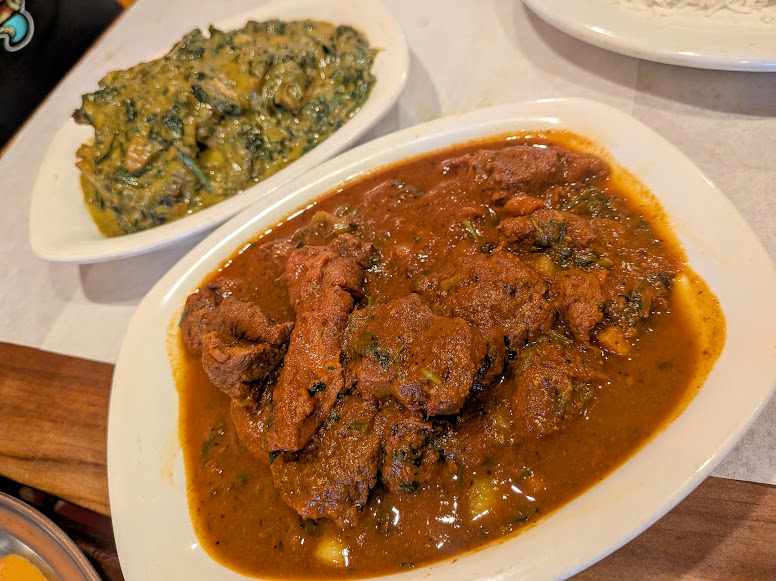 Two oval dishes: one with a thick, reddish-brown meat stew, the other with a creamy, green vegetable dish. Both are placed on a light-colored surface.