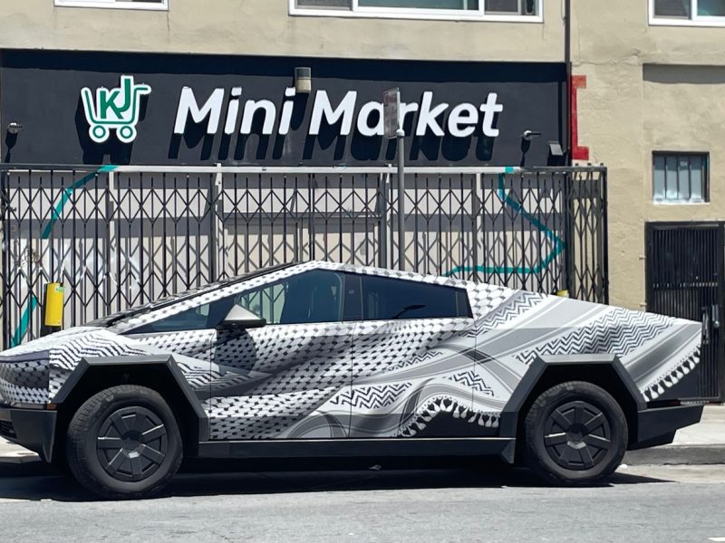 A geometric-patterned car with a futuristic design is parked on the street in front of a building with a "Mini Market" sign.