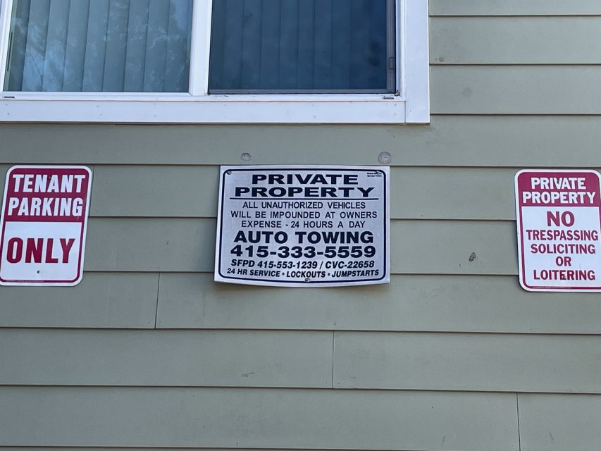 Three signs on a wall: "Tenant Parking Only," "Private Property" with towing details and phone number, and "No Trespassing, Soliciting or Loitering.