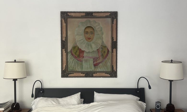 A framed painting of a person in ruffled attire hangs above a neatly made bed with white bedding, flanked by two lamps on bedside tables.