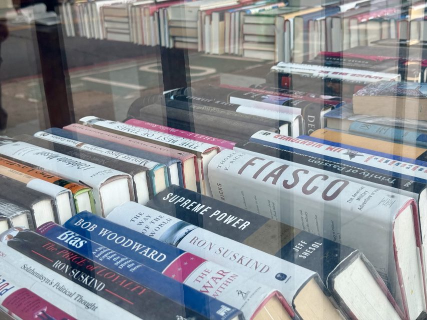 Books are displayed in a gallery window, with several titles and authors visible through the glass, including "Fiasco," "Supreme Power," and "The War Within.