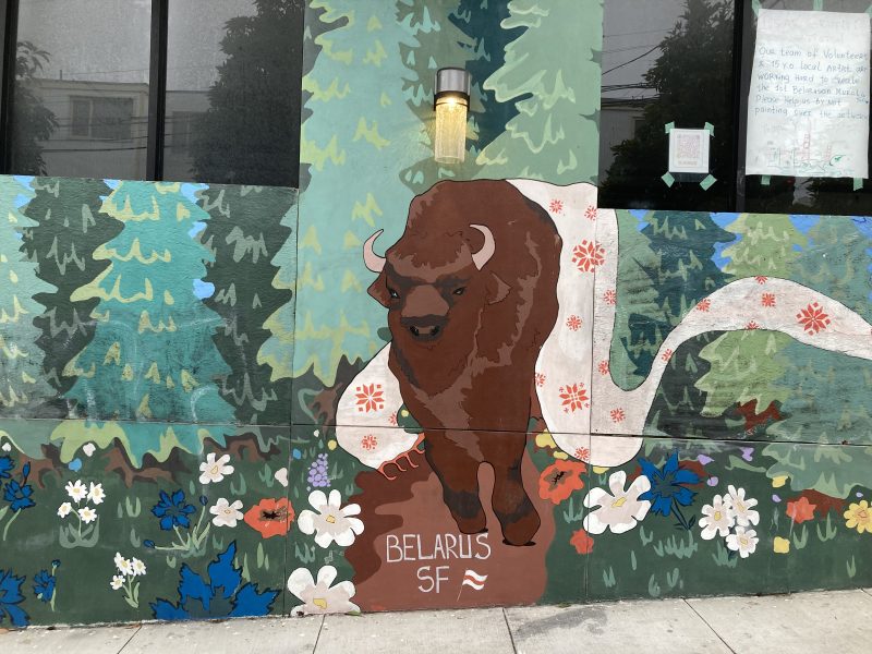 A mural of a bison with “BELARUS SF” written below, surrounded by trees and flowers, is painted on an exterior wall beneath a window.