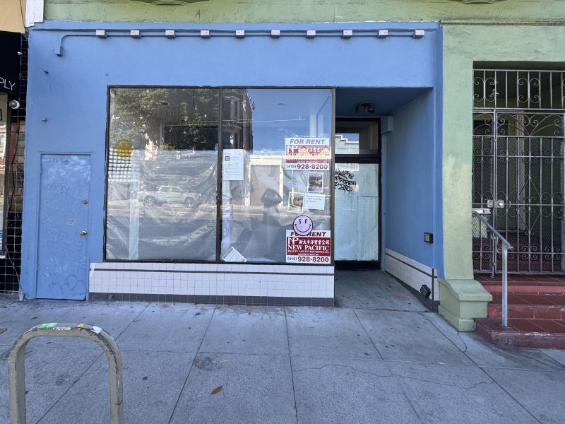 A vacant storefront with a blue facade displaying multiple "For Rent" signs in the window, located on a city sidewalk.