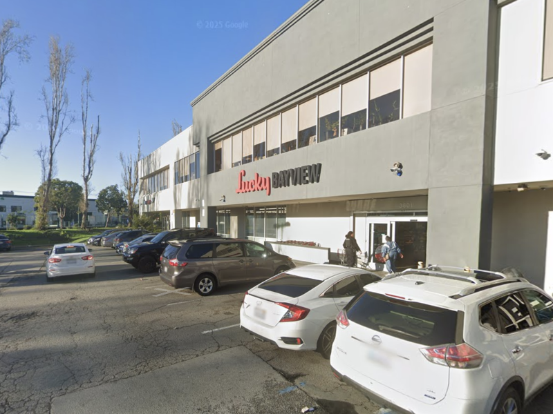 Parking lot in front of a Lucky Bayview grocery store, with several parked cars and people entering or exiting the store on a sunny day.