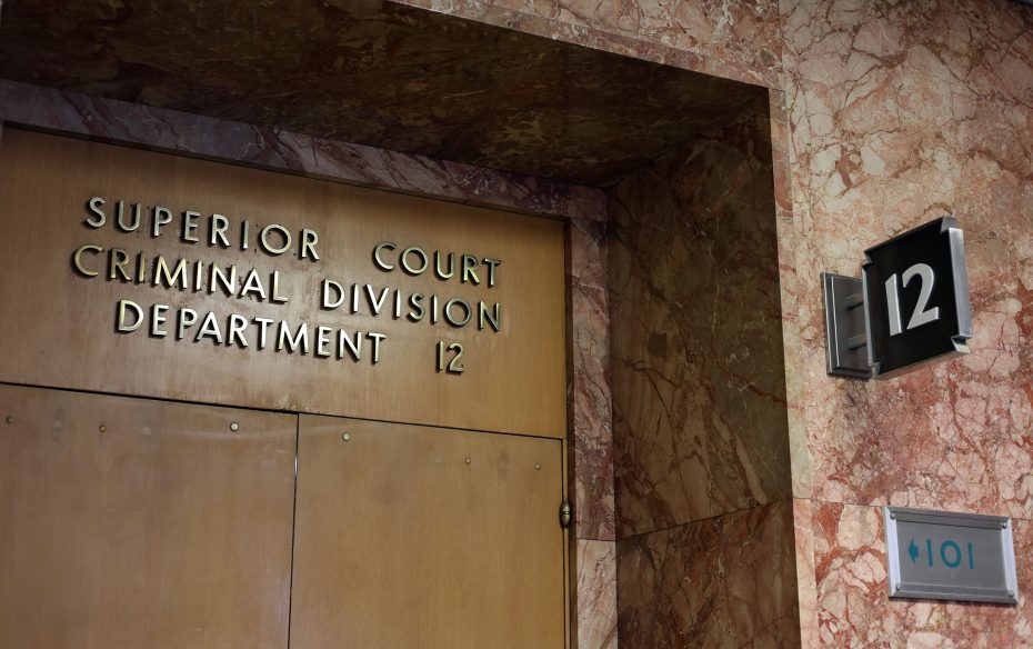 Brown double doors labeled "Superior Court Criminal Division Department 12" with a nearby sign showing the number 12 and a restroom symbol, set against a marble wall.