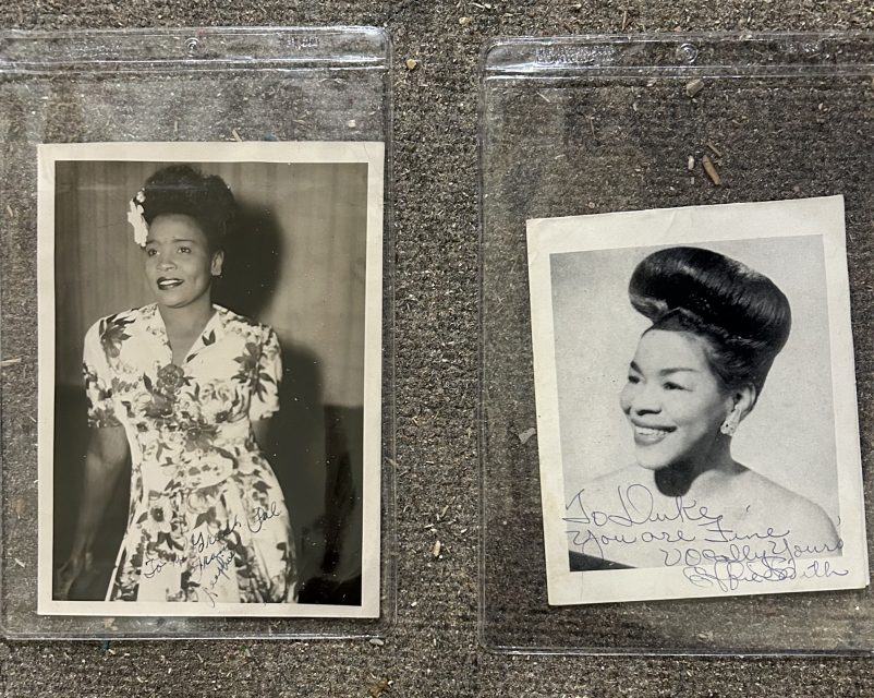 Two vintage black-and-white signed portraits of a smiling woman with an updo hairstyle, displayed in clear plastic sleeves on a textured surface.