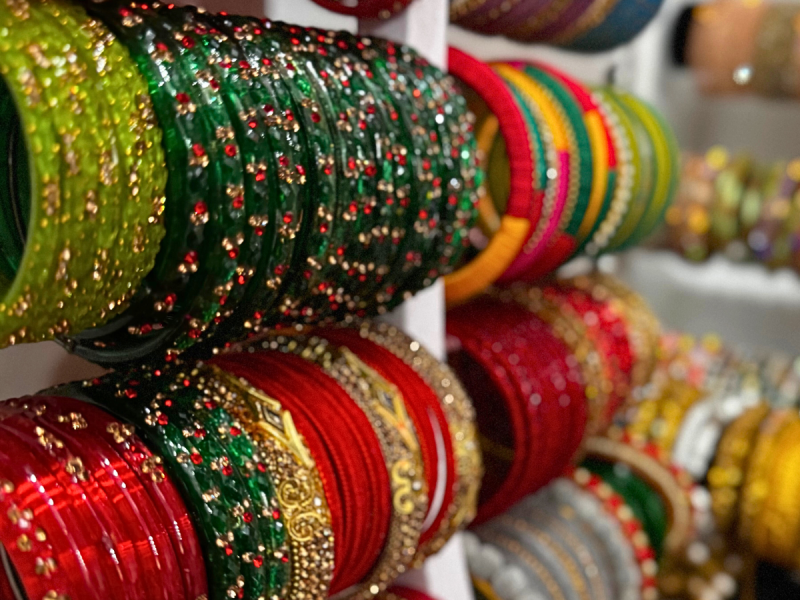 Rows of colorful, intricately designed bangles are displayed on stands, featuring red, green, gold, and other vibrant colors.