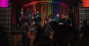 A jazz band performs on stage under colorful lights, with audience members dancing in the dimly lit foreground.