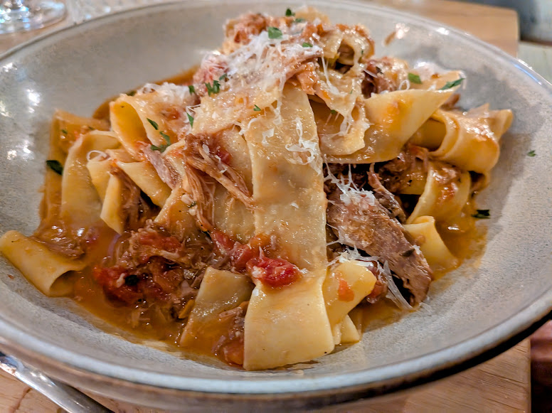 A bowl of pappardelle pasta topped with shredded meat, tomato sauce, and grated cheese.