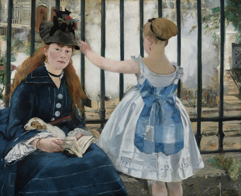 A woman with a small dog and a book sits beside a girl in a white dress with a blue sash, standing by a black iron fence.